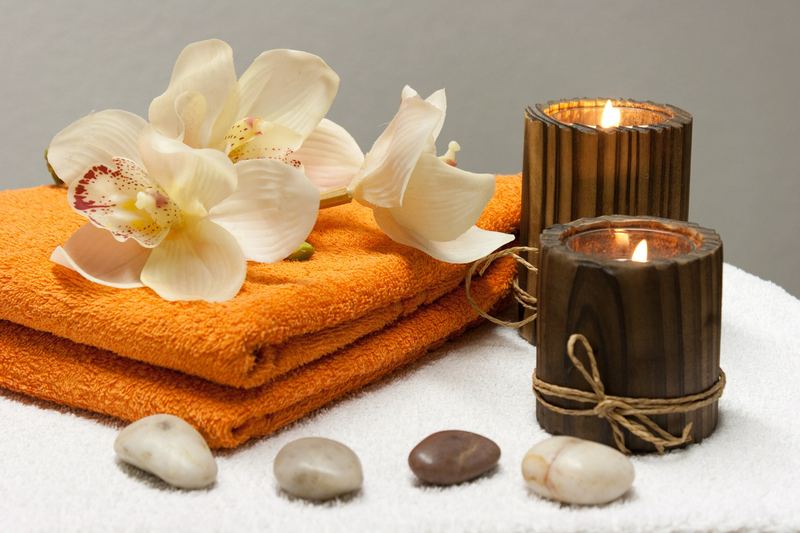 Ayurvedic spa setting with candles, orange towels, white flowers and massage stones